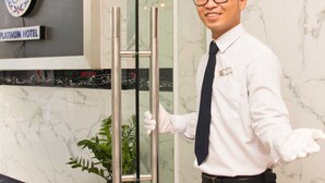 A hotel reception area with a marble wall, a sign for the Platinum Hotel, and a reception desk with a name tag. - The Noble Swan Hotel New World (Ho Chi Minh City)