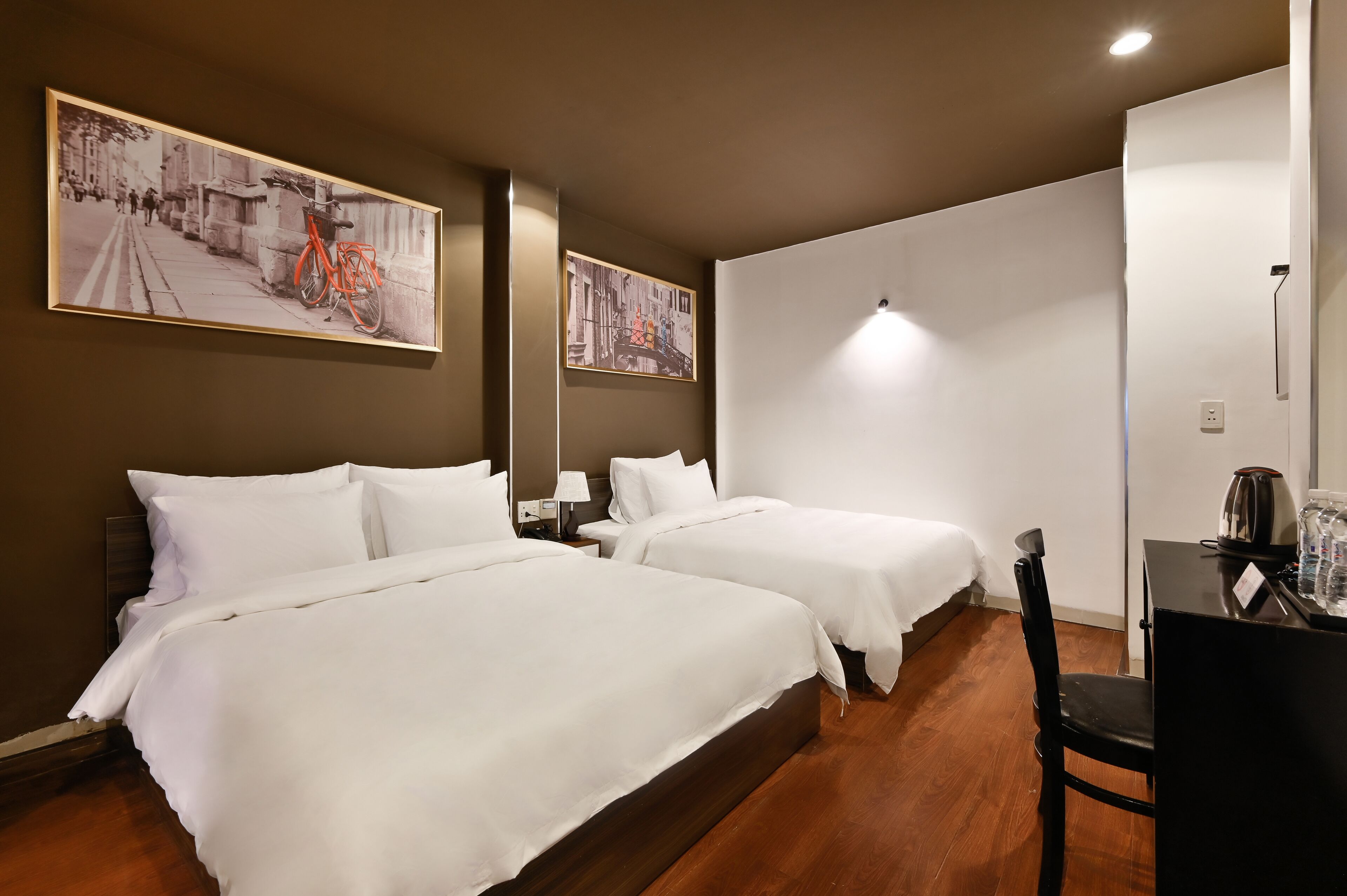 A hotel room with two beds, a desk, and two paintings on the wall.