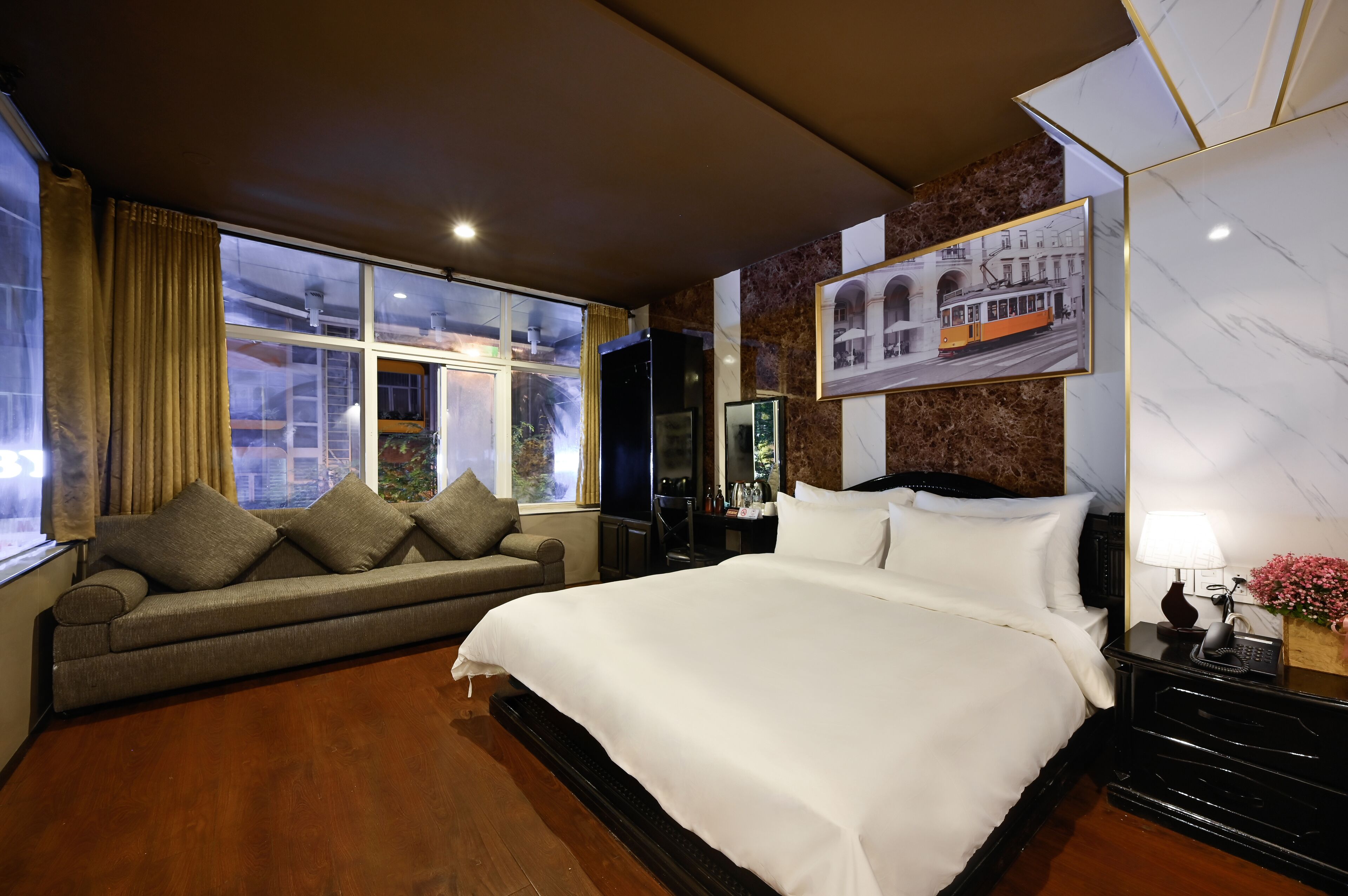A hotel room with a large bed, a sofa, a TV, and a window with a city view.