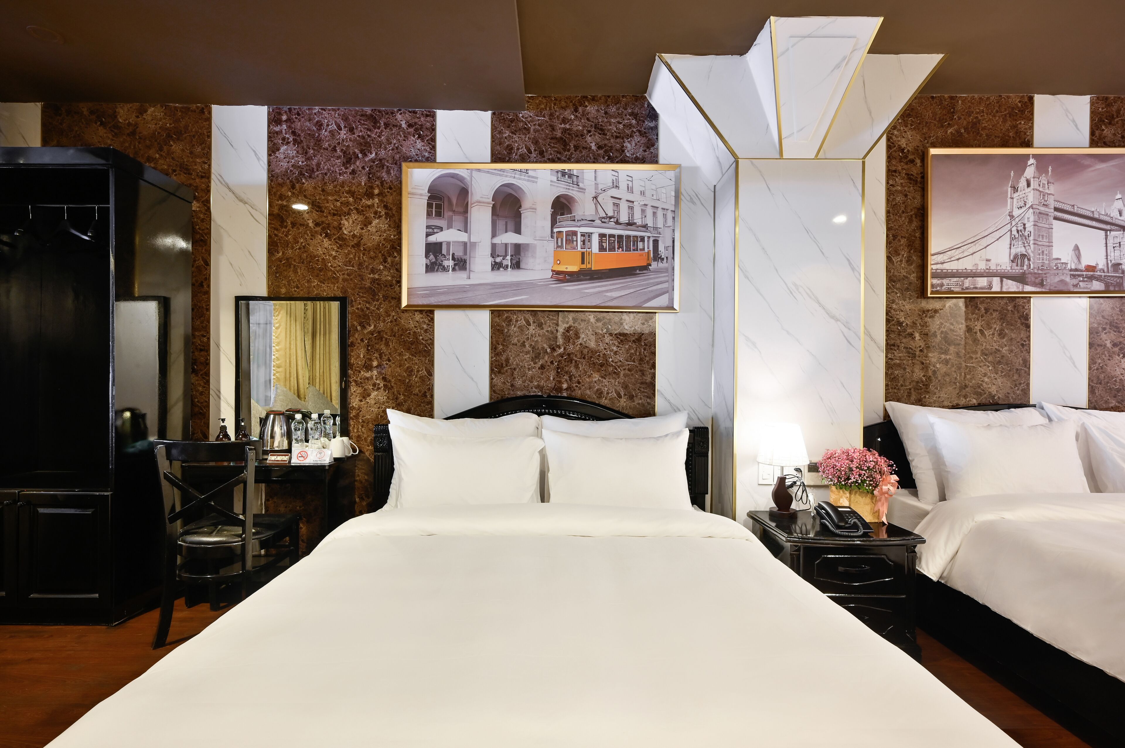Ein Hotelzimmer mit einem großen Bett, einem Schreibtisch mit Lampe, einem Sessel und zwei gerahmten Bildern von Brücken.