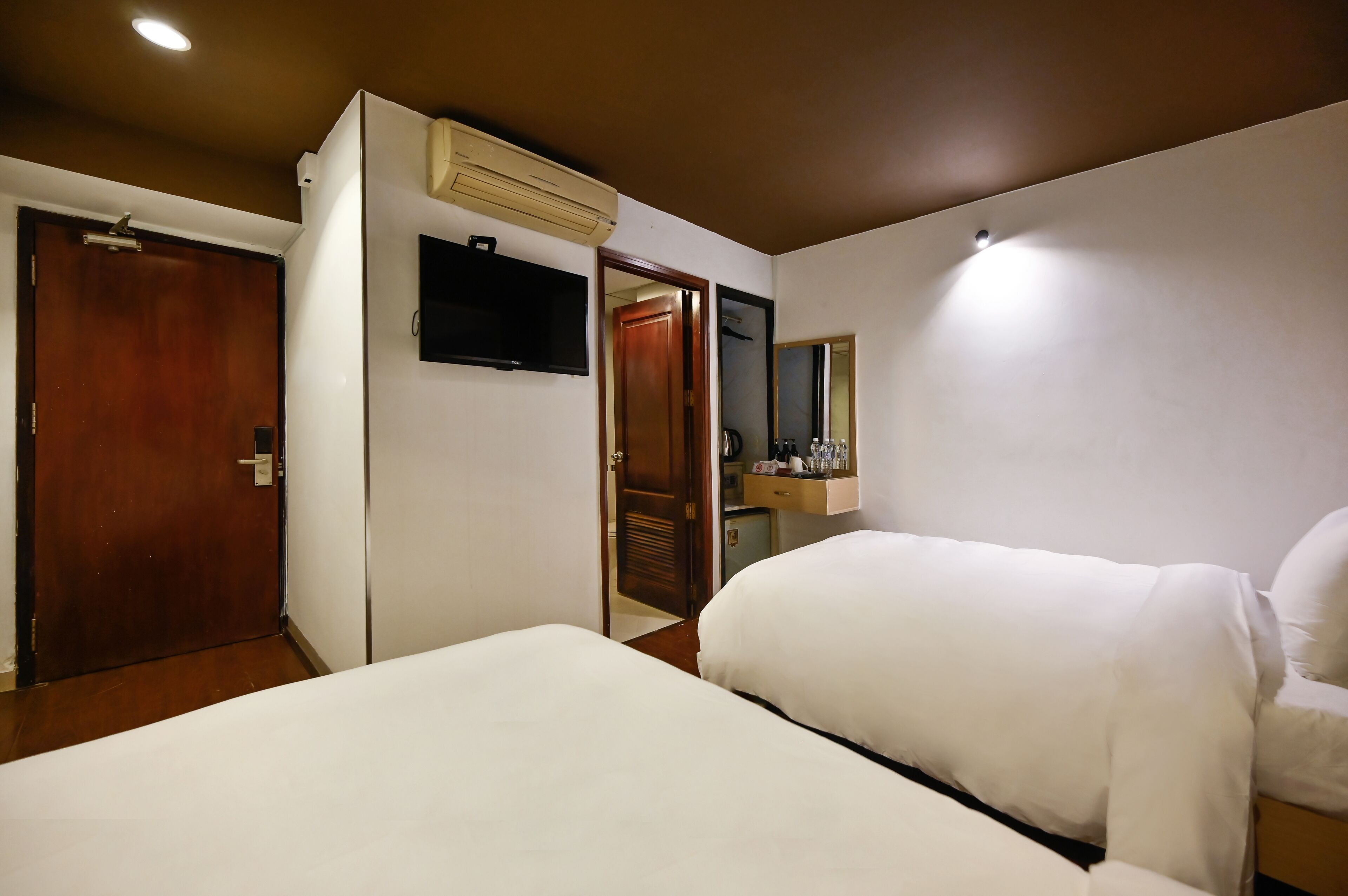 A hotel room with two beds, a television, a mirror, and a wardrobe.