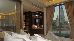 A hotel room with a large bed, a glass shower enclosure, a minibar, and a view of a cityscape. - Braira Hotel Olaya (Riyadh)