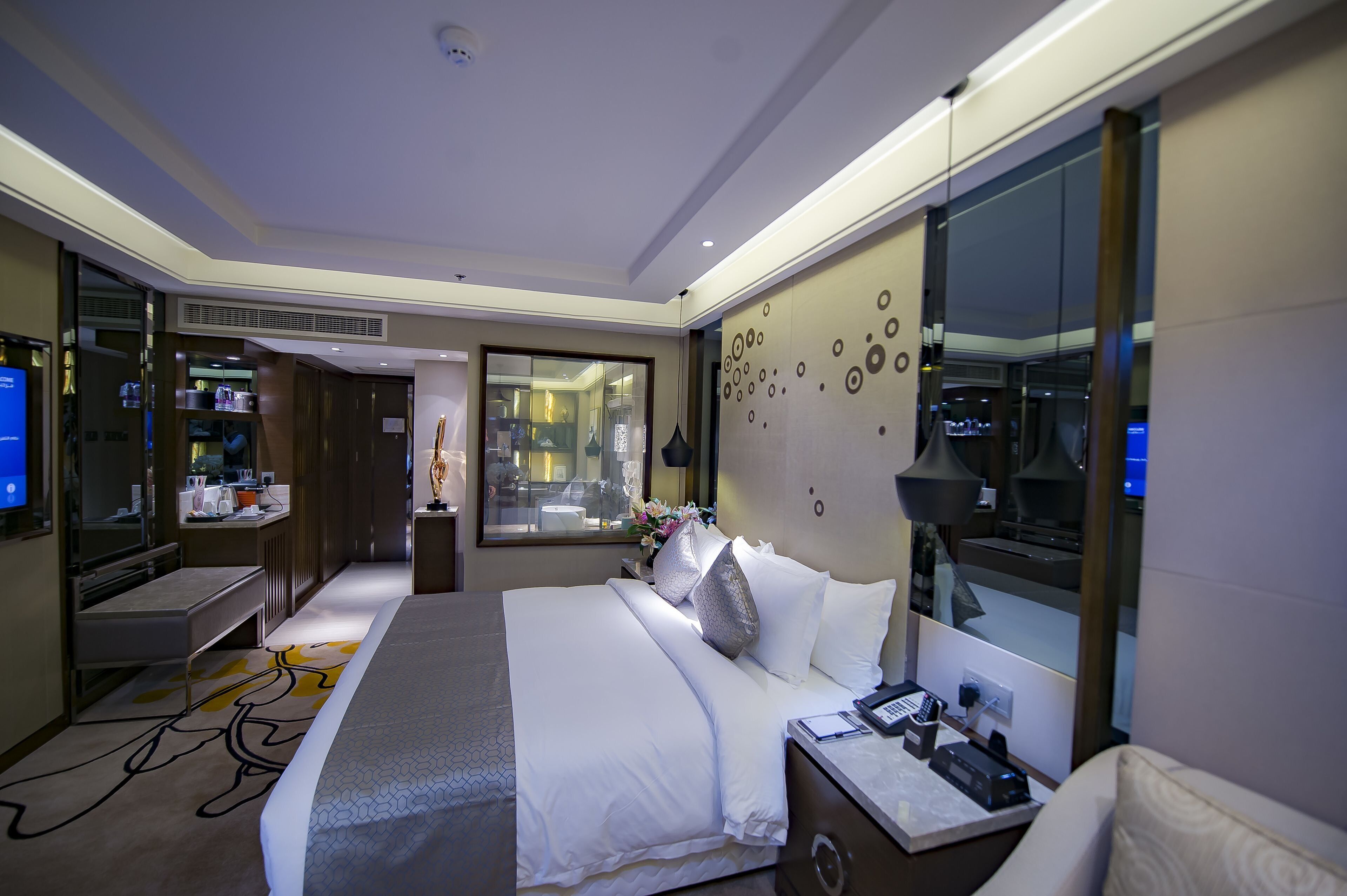 Habitación de hotel con una cama grande, mesita de noche y un escritorio con una silla. Se ve una ventana con vistas a la ciudad.
