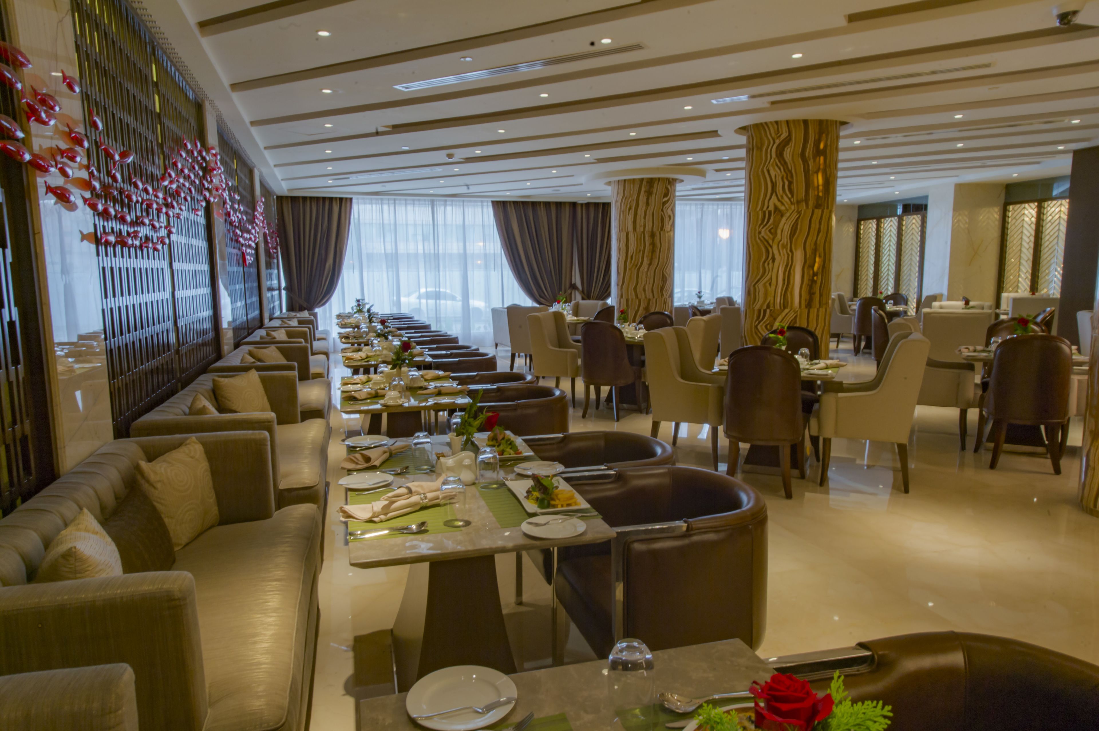 A spacious dining area with multiple tables and chairs, a long counter, and a decorative wall with hanging elements.