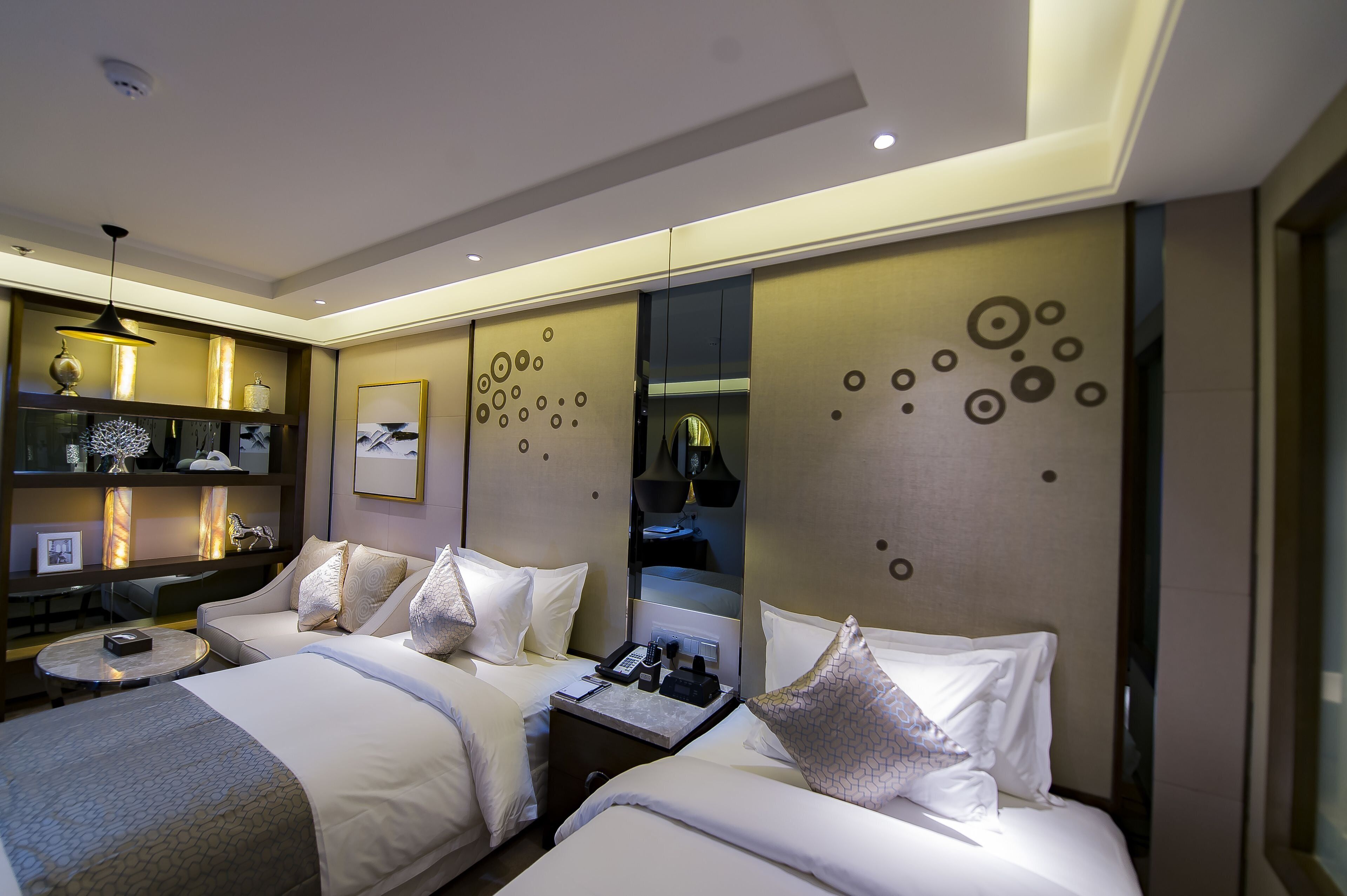 A hotel room with two beds, a bedside table with a lamp, a mirror, and a decorative wall with circular patterns.
