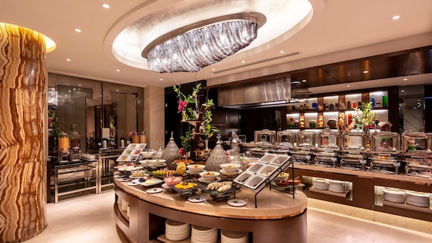 A buffet area with a central island, a chandelier, and a modern kitchen in the background. - Braira Hotel Olaya (Riyadh)