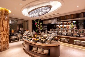 A buffet area with a central island, a chandelier, and a modern kitchen in the background. - Braira Hotel Olaya (Riyadh)