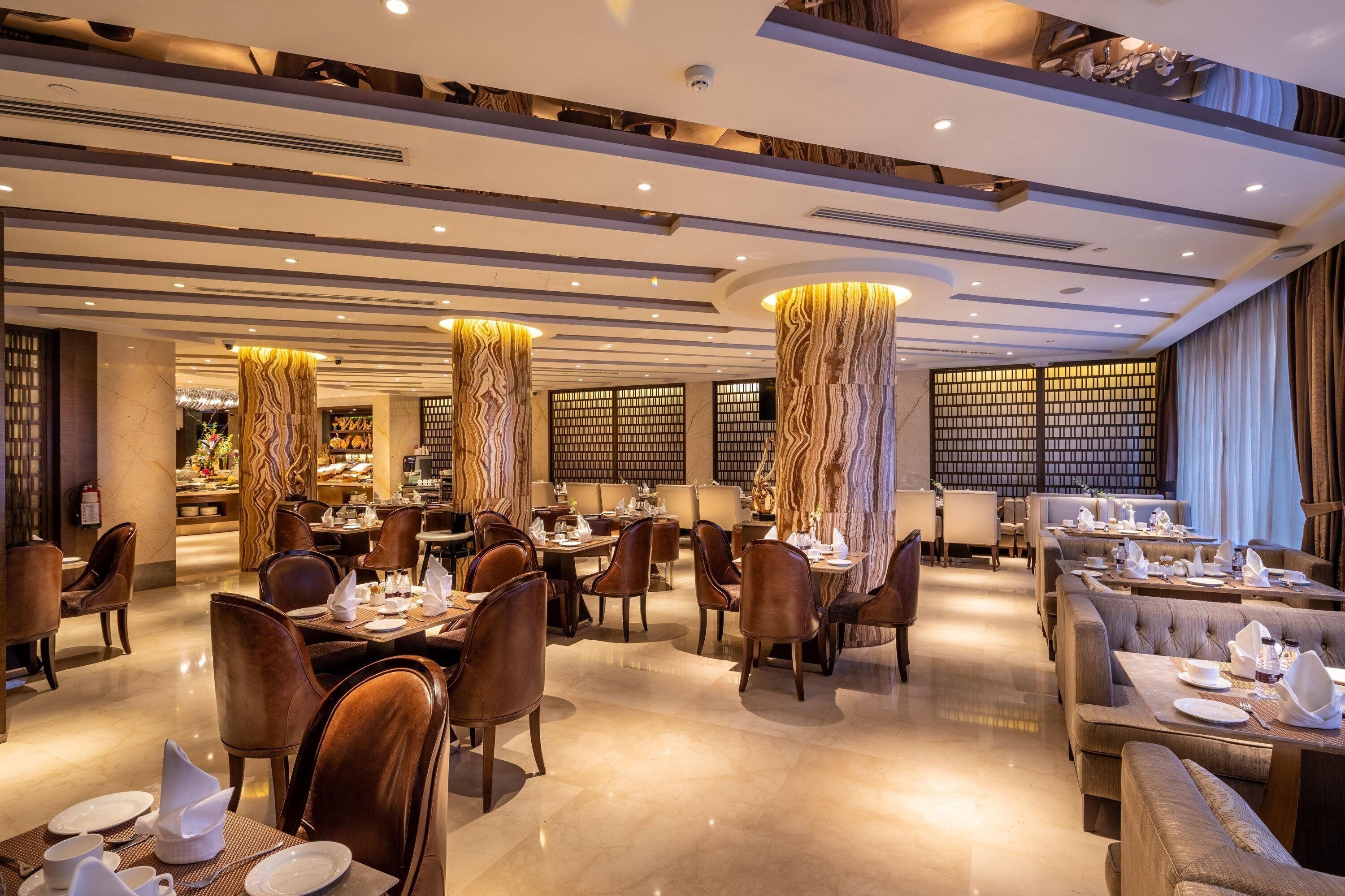 Een ruim restaurant met hoge plafonds, modern verlichtingsarmaturen en diverse zitplaatsen, waaronder tafels en zitbanken.