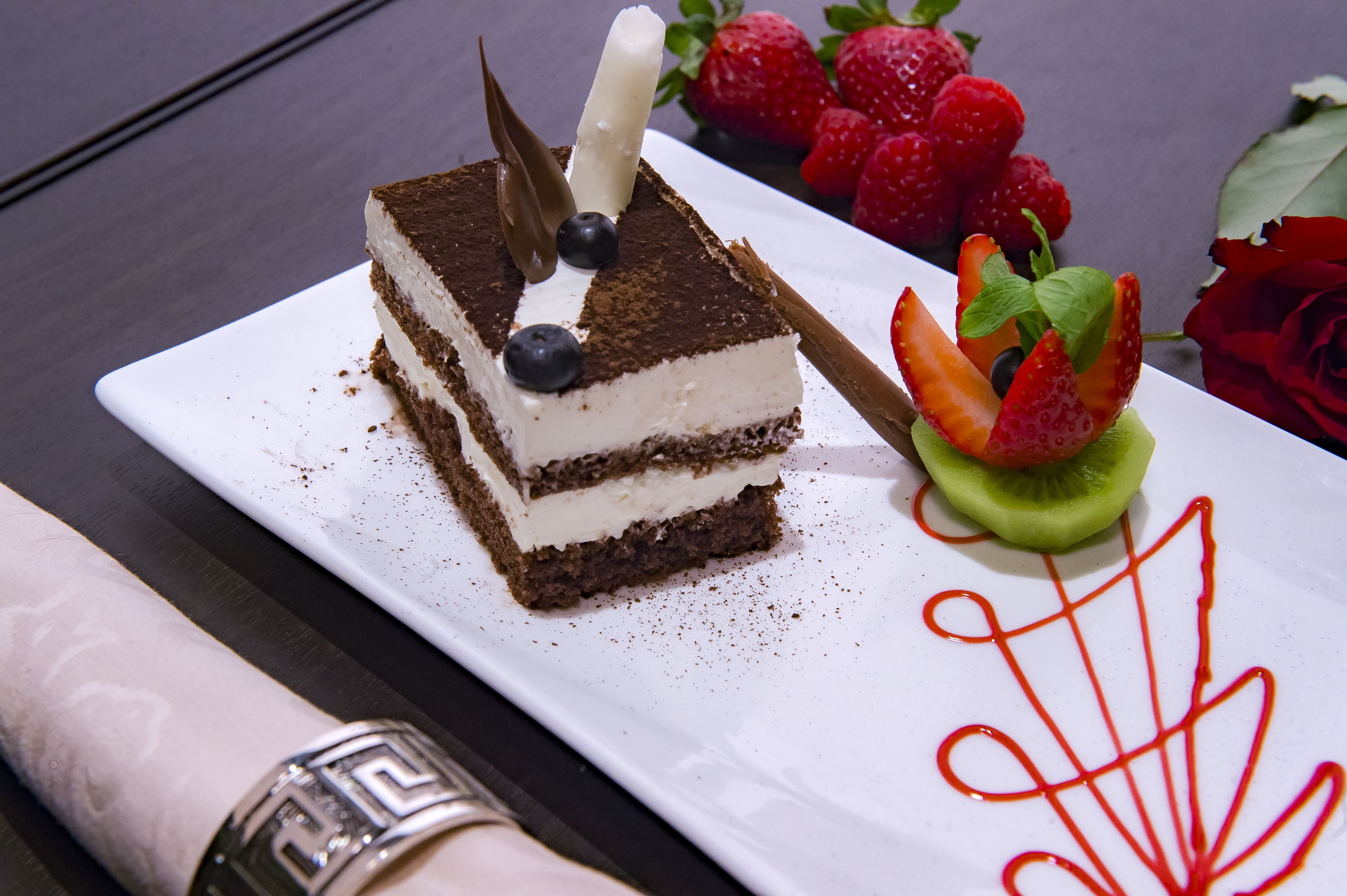 A slice of layered cake with strawberries and a rose on a white plate.