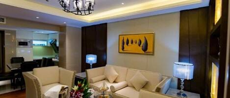A modern hotel room with a sofa set, a dining table with flowers, a lamp, and a painting on the wall.