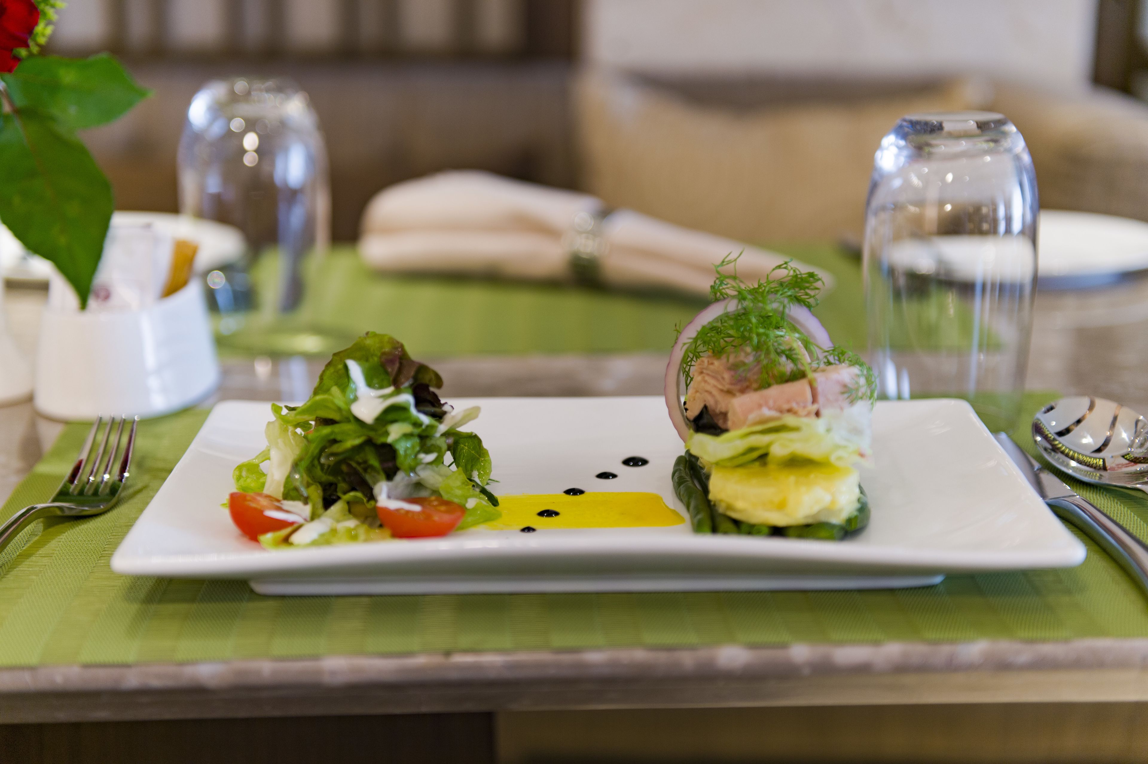 A neatly arranged dining table with a white plate of food, a green placemat, and a clear glass of water.