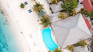 An aerial view of a beach resort with a swimming pool, lounge chairs, and thatched-roof structures. - Sudamala Resort, Seraya, Flores (Labuan Bajo)