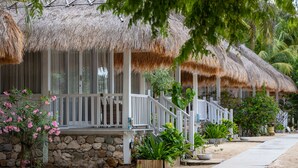 A row of thatched-roof cottages with white railings and stone walls, surrounded by tropical plants and a paved walkway. - Sudamala Resort, Seraya, Flores (Labuan Bajo)