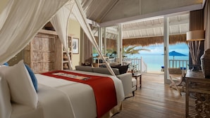A bedroom with a bed, a wooden floor, a balcony with a view of the sea, and a thatched roof. - Sudamala Resort, Seraya, Flores (Labuan Bajo)