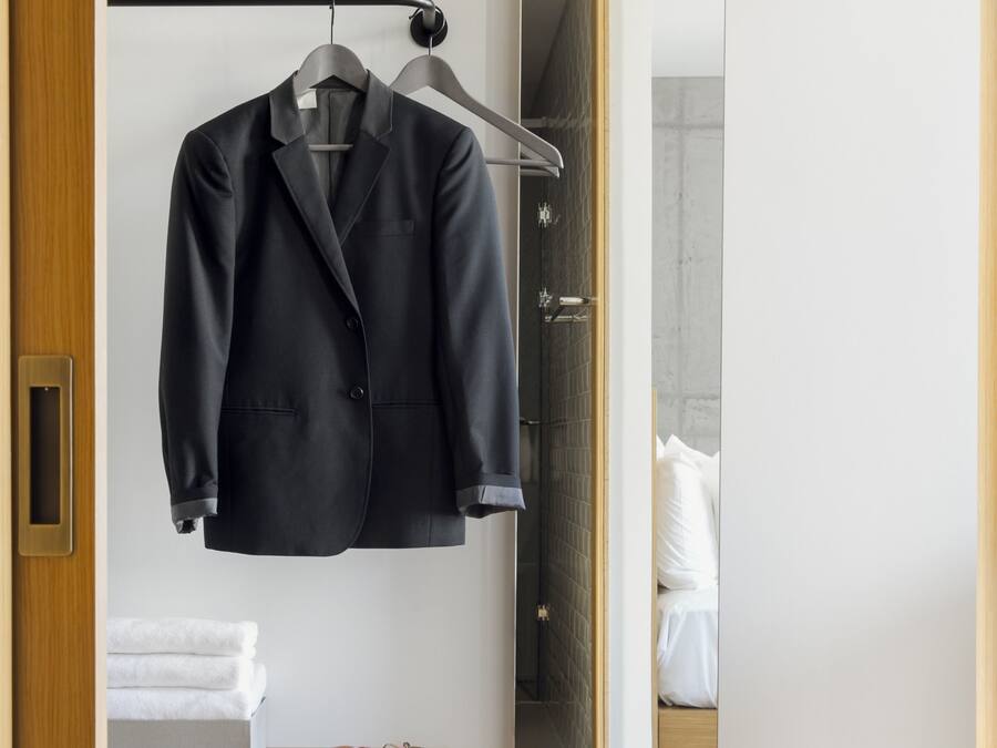 A neatly organized bedroom with a hanging coat rack, a bedside table with a plant, and a visible emergency box.
