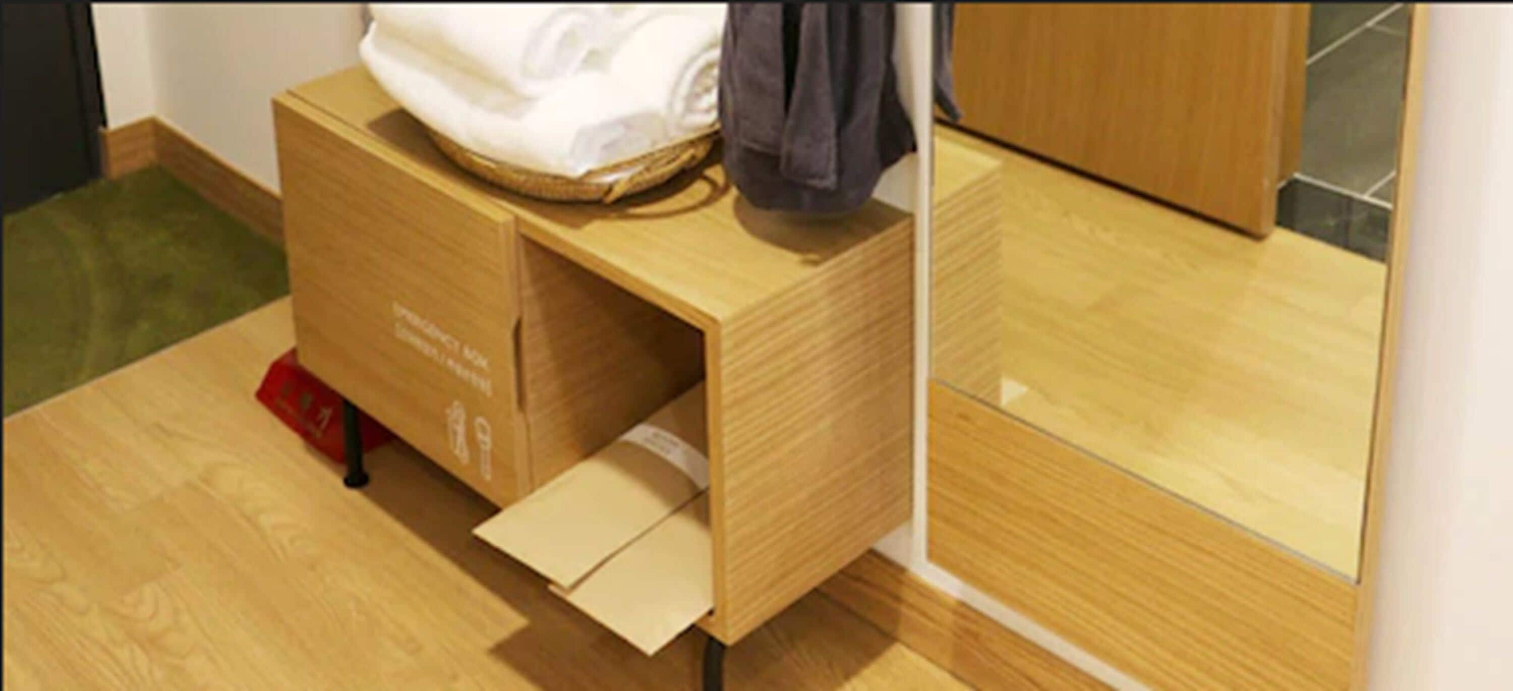 Un mueble de madera con un cajón, un objeto rojo en el suelo y una bolsa blanca encima.
