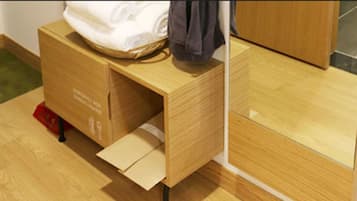 A wooden cabinet with a drawer, a red object on the floor, and a white bag on top.