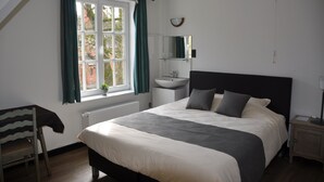 Une chambre à coucher comprenant un lit, une table de chevet, une chaise, une fenêtre avec des rideaux, un miroir et une petite plante.