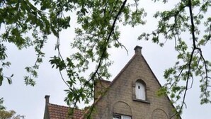 Un bâtiment à deux étages, construit en briques, avec un toit à forte pente, de nombreuses fenêtres et un auvent vert au-dessus de l’entrée.