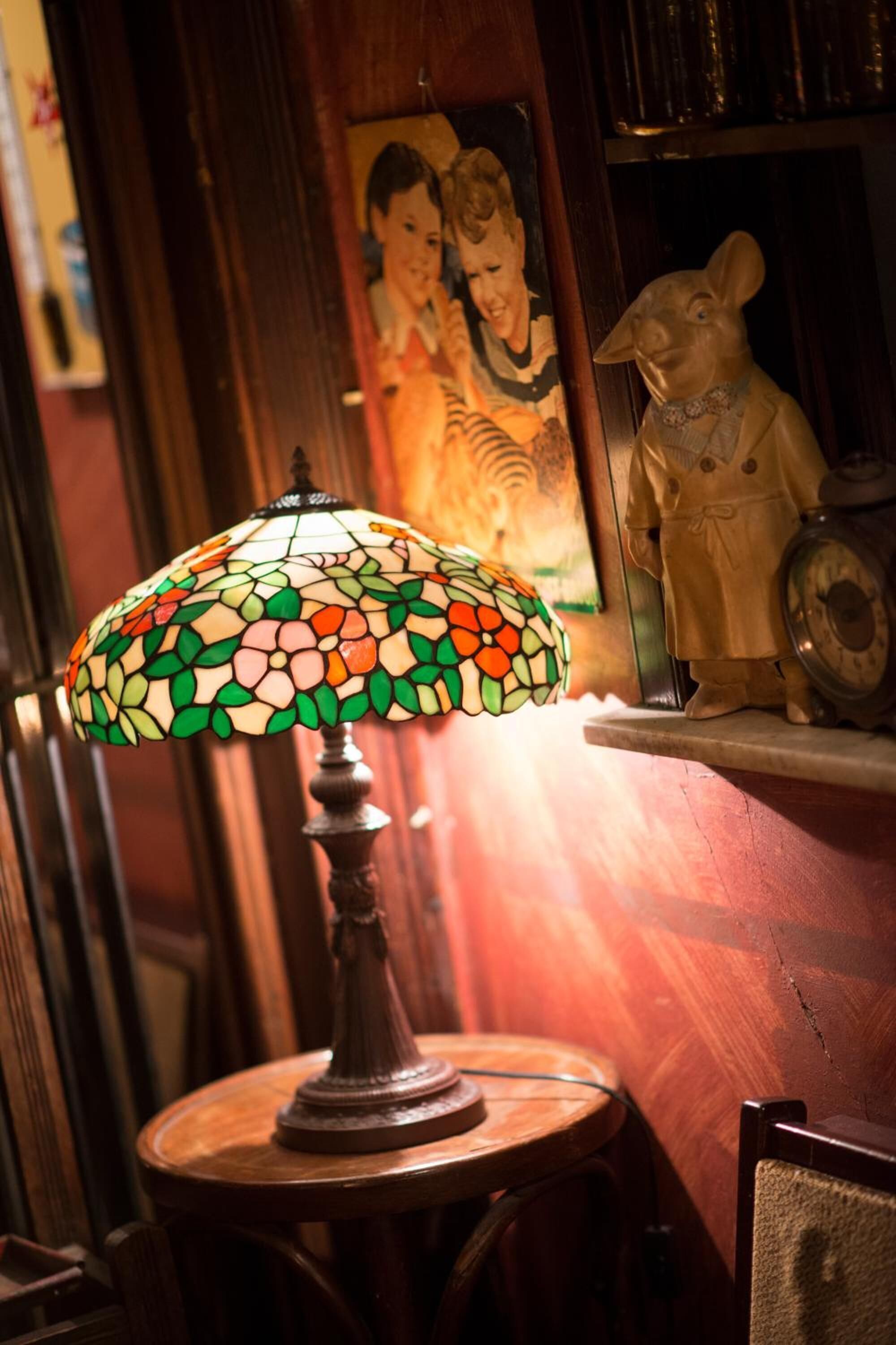 A stained glass lamp on a wooden table, a framed picture on the wall, and a piggy bank on a shelf.