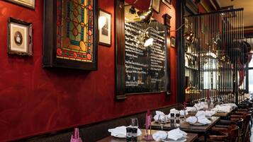 A restaurant with red walls, framed pictures, and a long table set for dining.