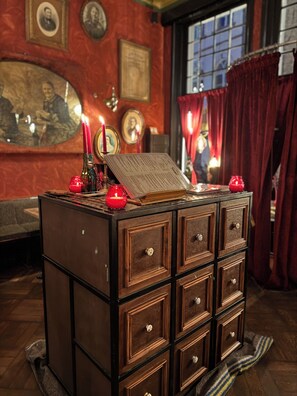 A wooden chest with drawers, candles, and framed pictures on a wall. - Gran Hotel de Passage (Bruges)