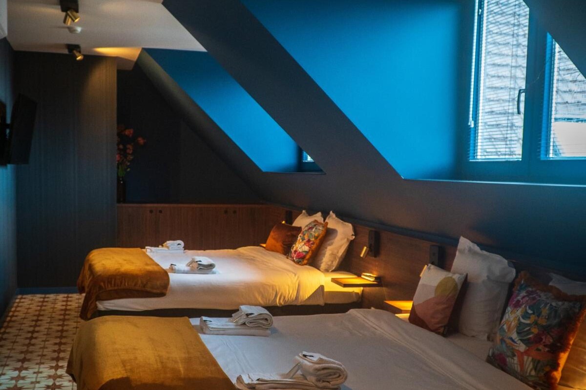 A hotel room with two beds, a sloped ceiling, and a large window.