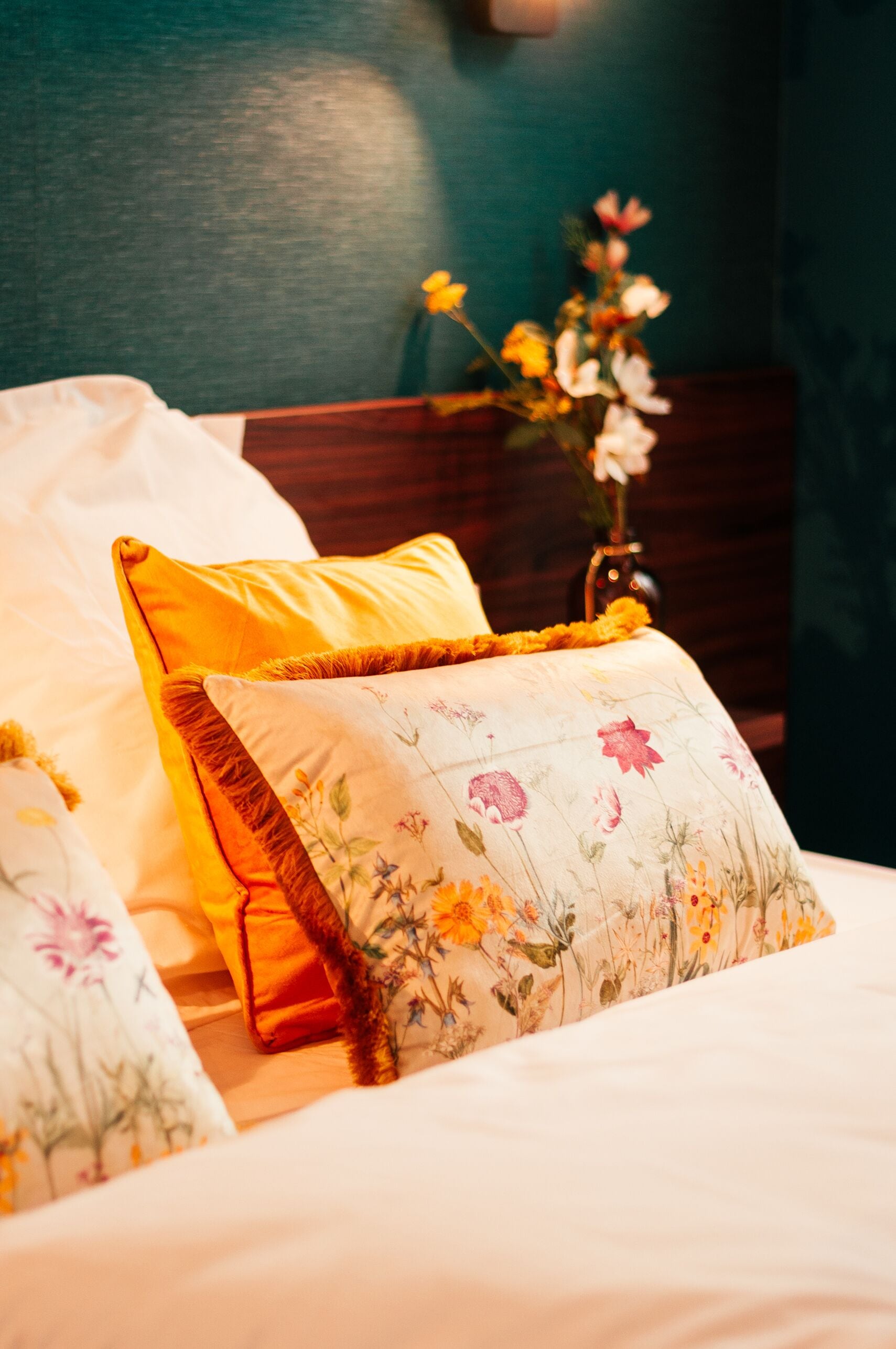 A neatly made bed with floral-patterned pillows and a vase with flowers.