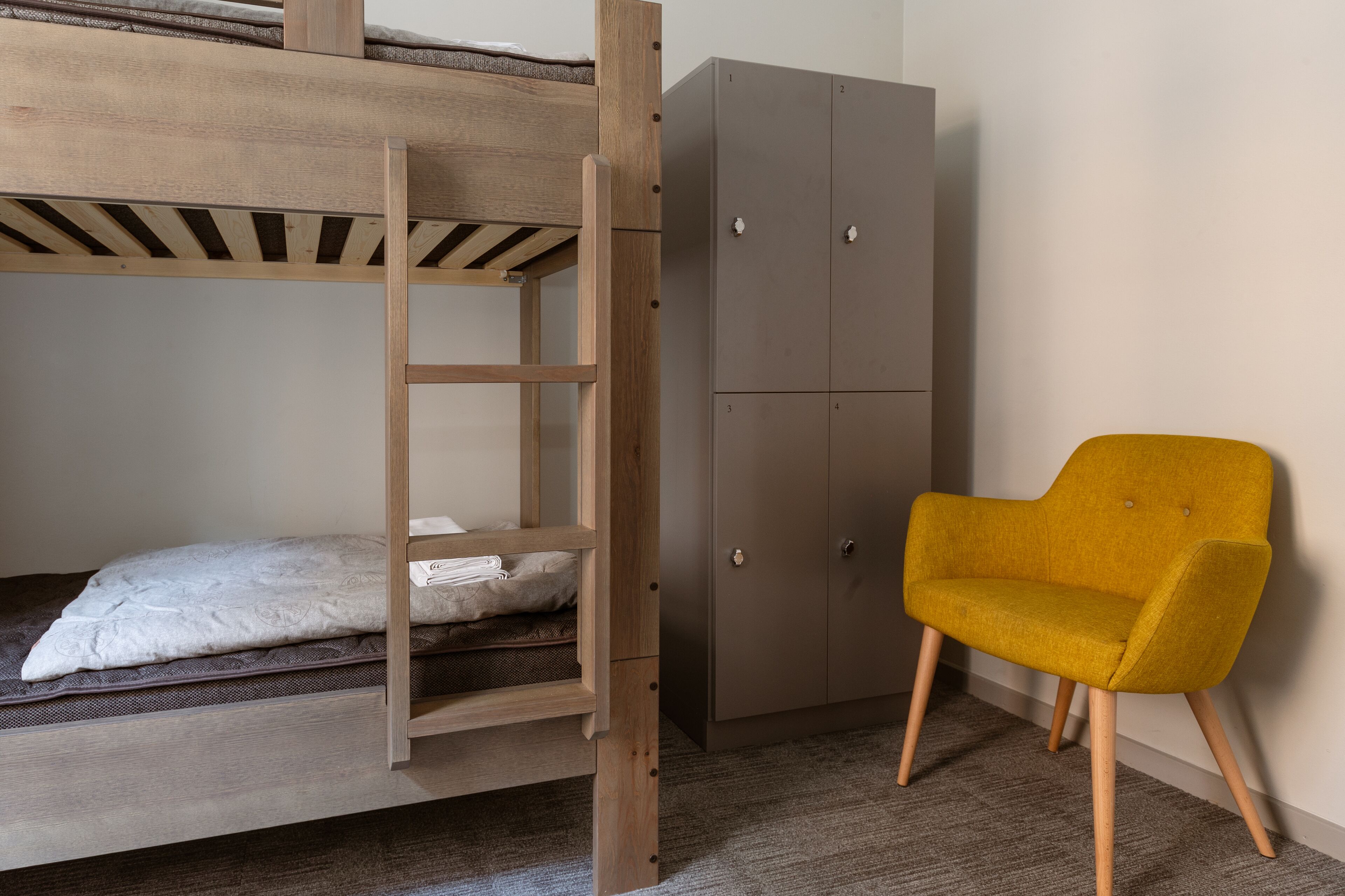 Ein Etagenbett mit Holzleiter, ein grauer Kleiderschrank und ein senfgelber Sessel.