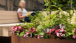 Eine Frau sitzt auf einer Bank vor einem Blumenbeet.