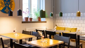 Ein Restaurantinneres mit mehreren Tischen und Stühlen, Pendelleuchten, Blumentöpfen und einem Fenster mit Blick nach draußen.