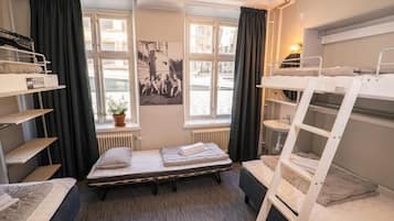 A dormitory room with bunk beds, a window with curtains, a radiator, and a poster on the wall.