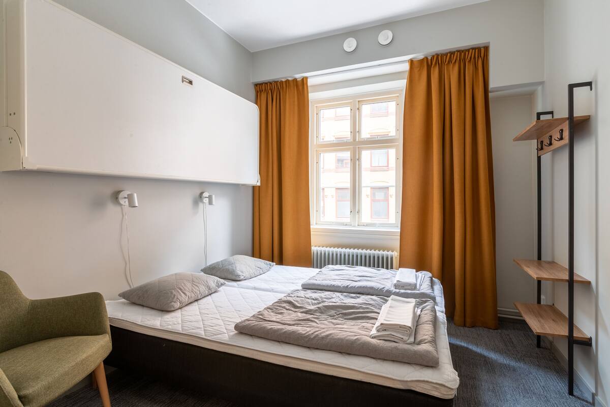 A single bed with a headboard, a bedside table, a chair, and a window with curtains.