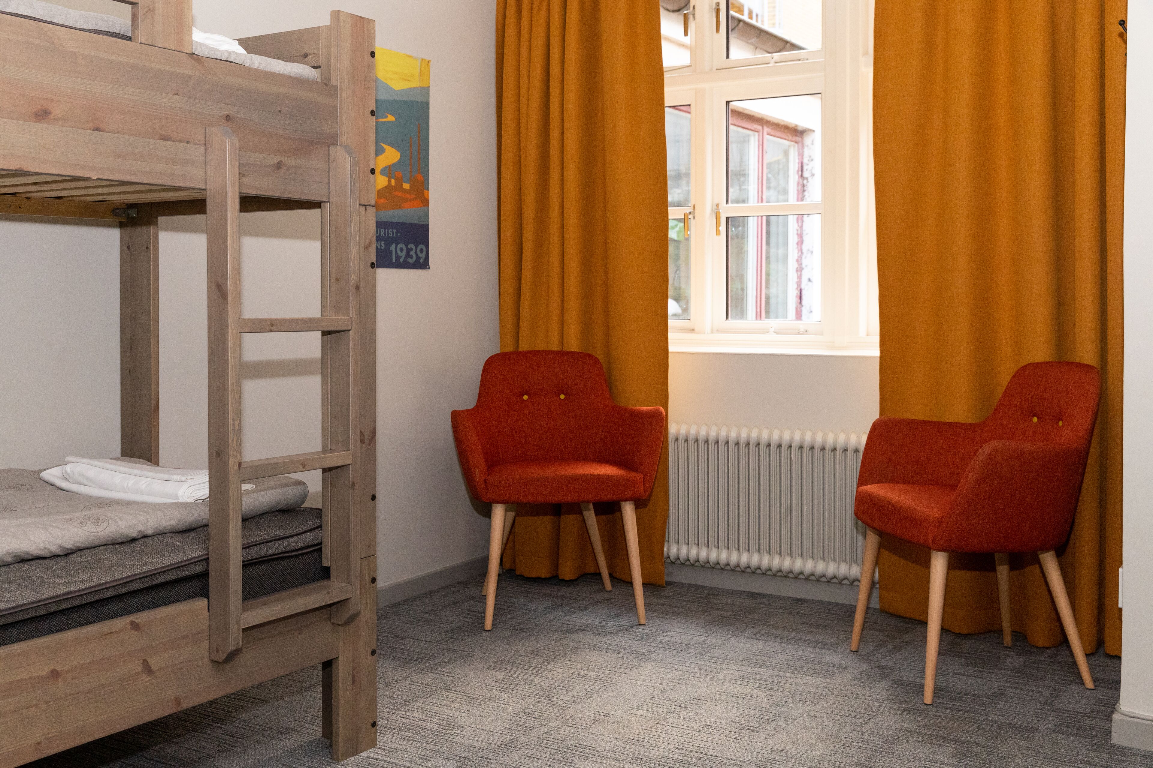 A bunk bed with a poster, two red chairs, a window with yellow curtains, and a radiator.