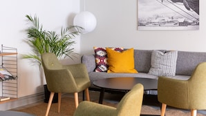 Ein modernes Wohnzimmer mit einem grauen Sofa, grünen und gelben Sesseln, einem runden Couchtisch und einer großen Topfpflanze.