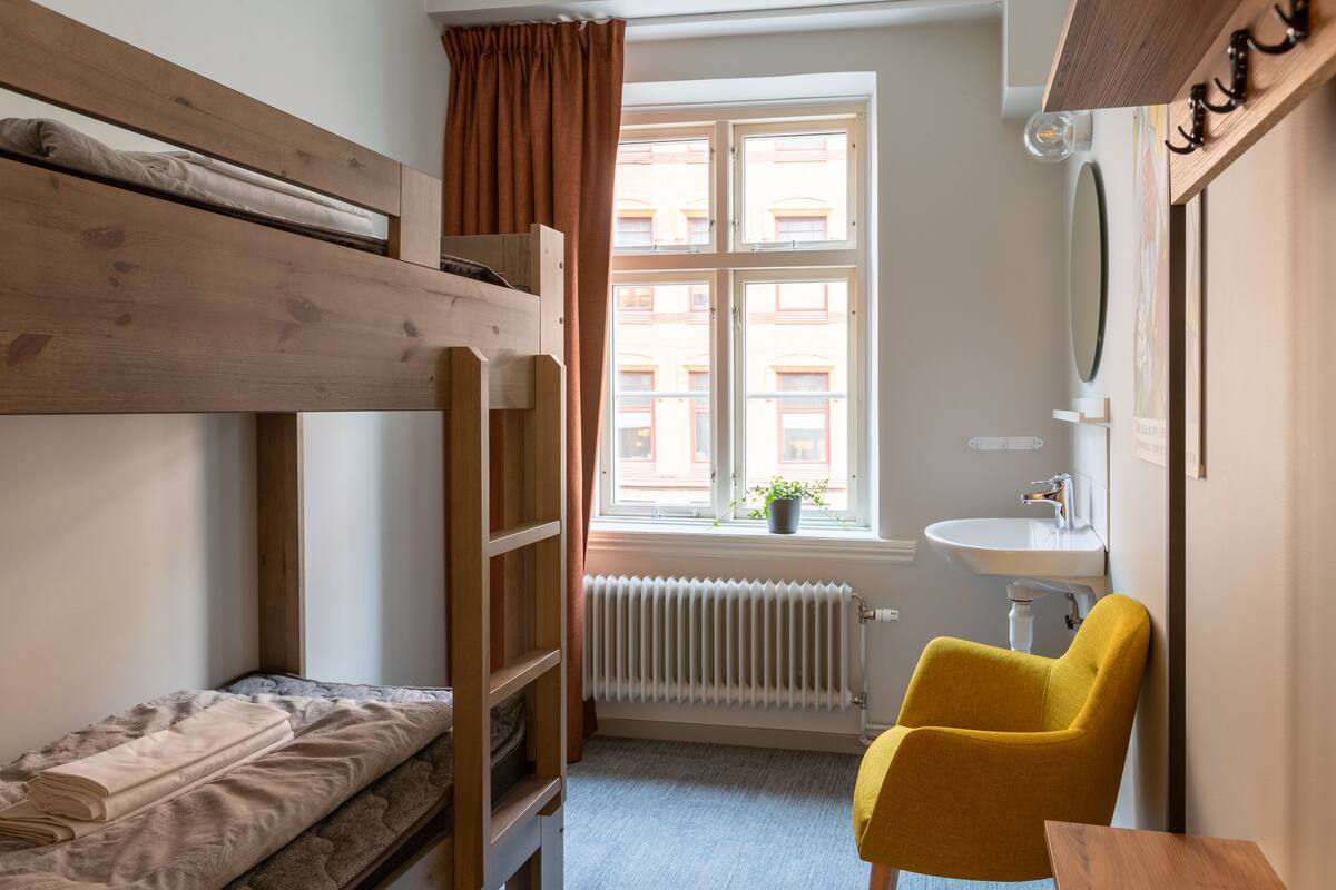 A bunk bed room with a window, a radiator, a sink, and a yellow chair.