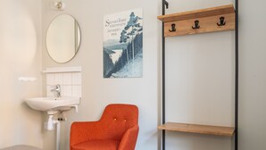 Ein Schlafzimmer mit einem Bett, einem weißen Waschbecken, einem orangefarbenen Sessel, einem Holzregal und einem Poster an der Wand.
