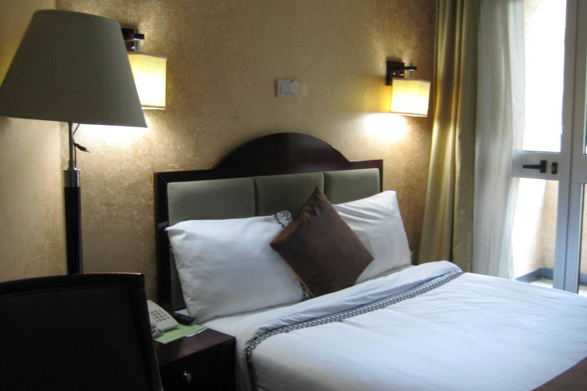 A hotel room with a bed, a nightstand with a lamp, and two wall-mounted lights.