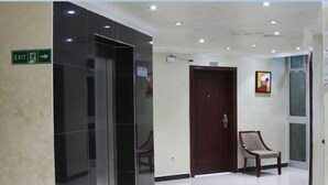 Um corredor com sinalização de saída, uma porta de madeira, uma cadeira e uma televisão fixada na parede.