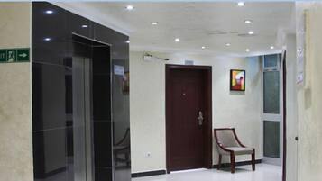 A hallway with an exit sign, a wooden door, a chair, and a wall-mounted television.