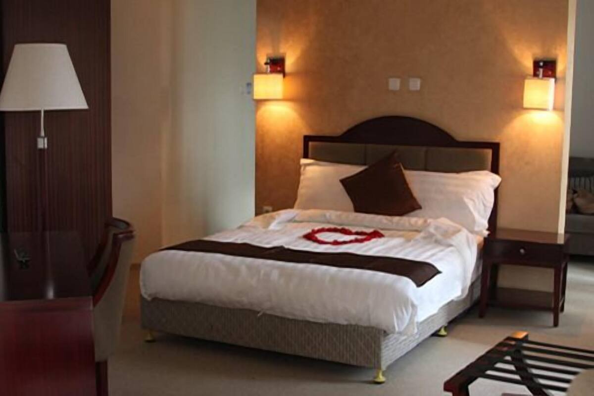 A neatly made bed with a heart-shaped decoration, a bedside lamp, and two wall-mounted lamps.