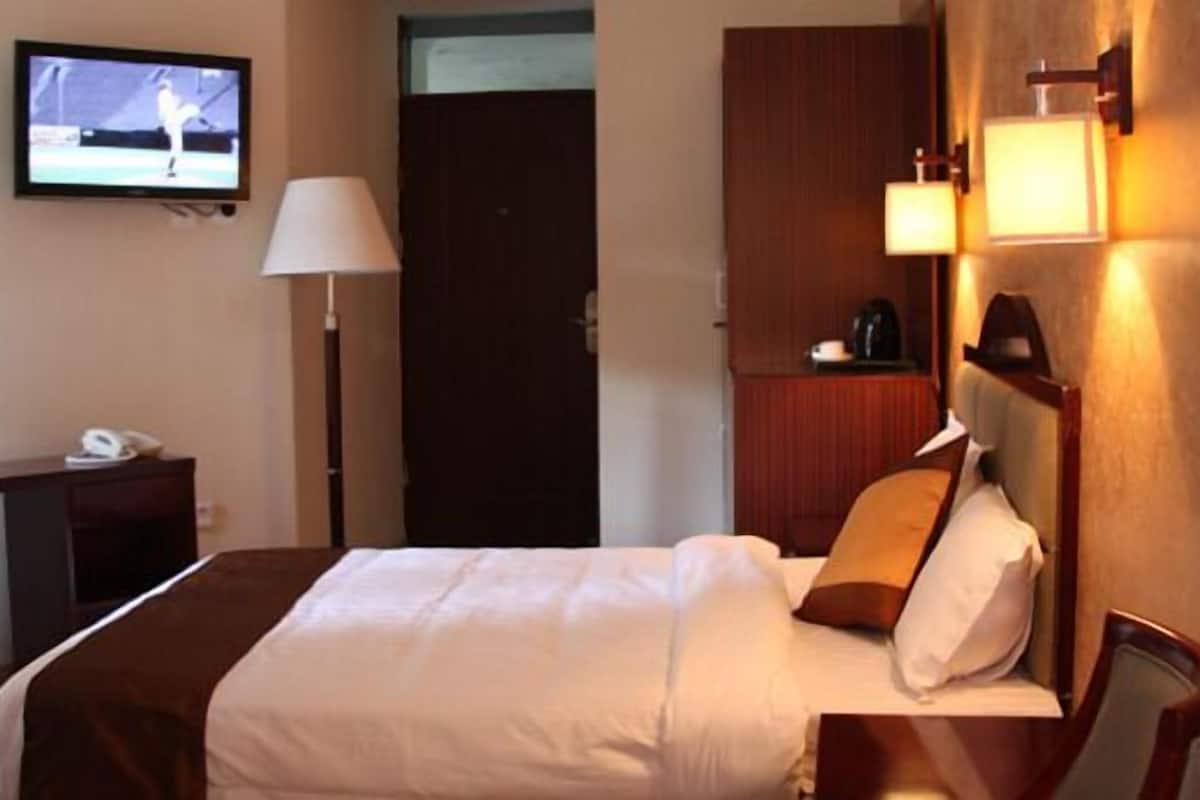 A hotel room with a bed, a desk, a television, a lamp, and a nightstand.
