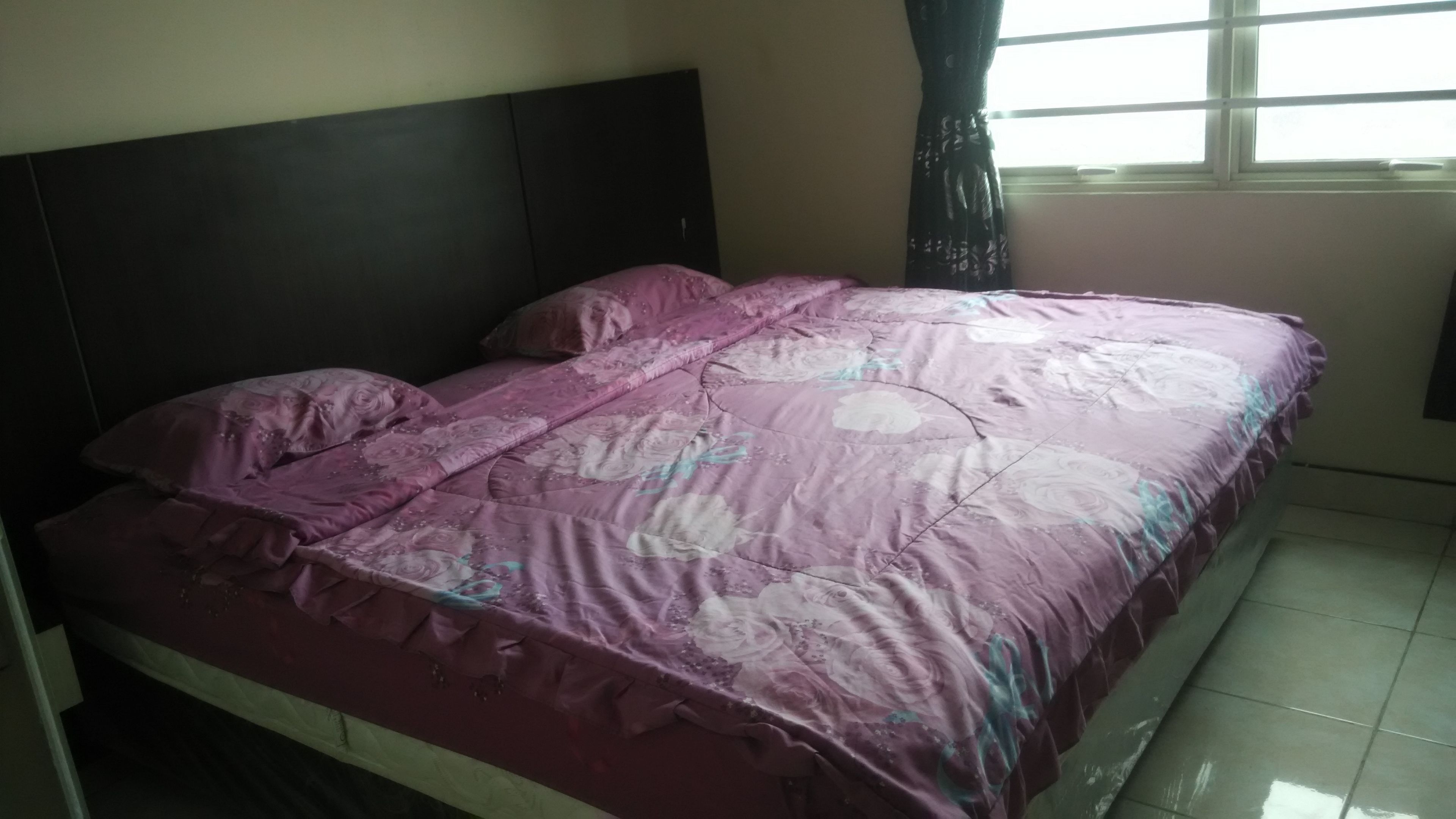 A bed with a floral bedspread, a dark headboard, and a window with curtains.