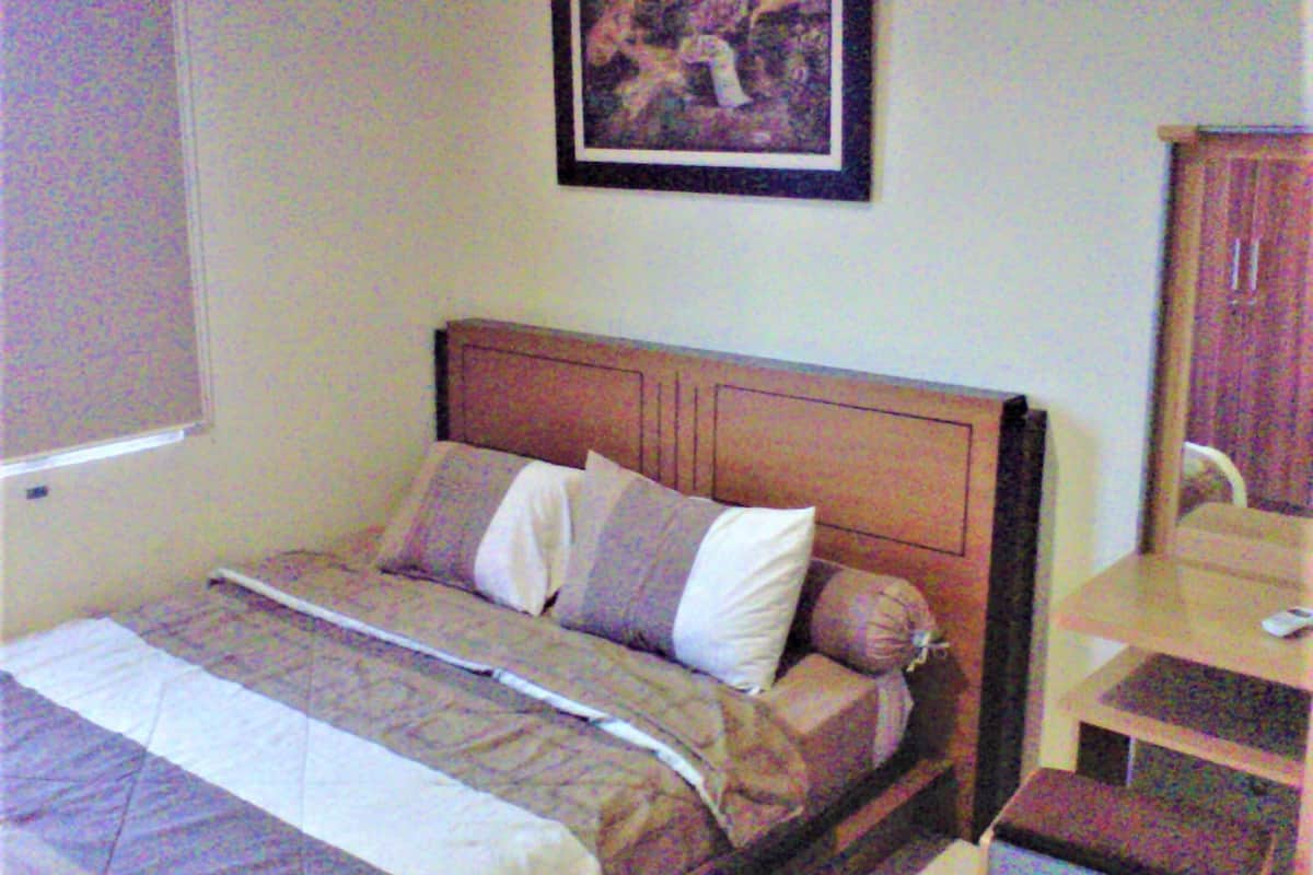 A bedroom with a bed, pillows, a headboard, a nightstand, and a framed picture on the wall.