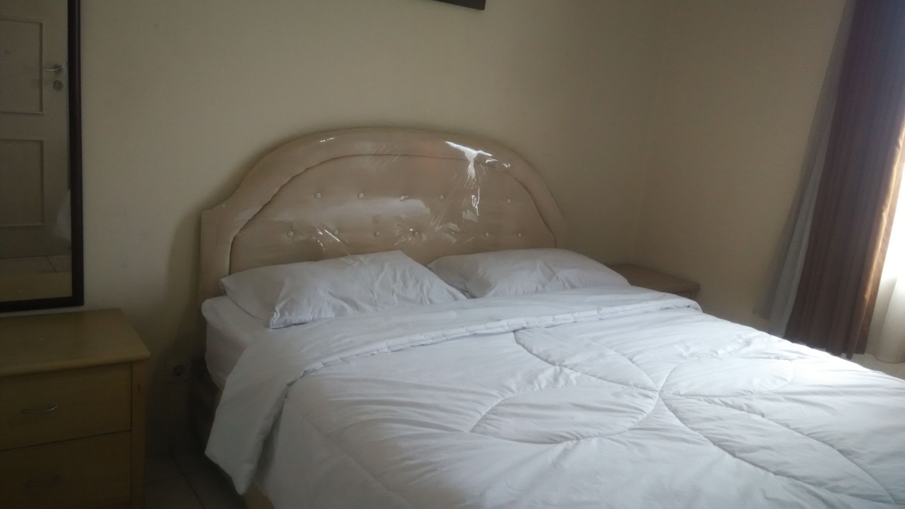 A bed with a headboard, white bedding, and a nightstand with a drawer.