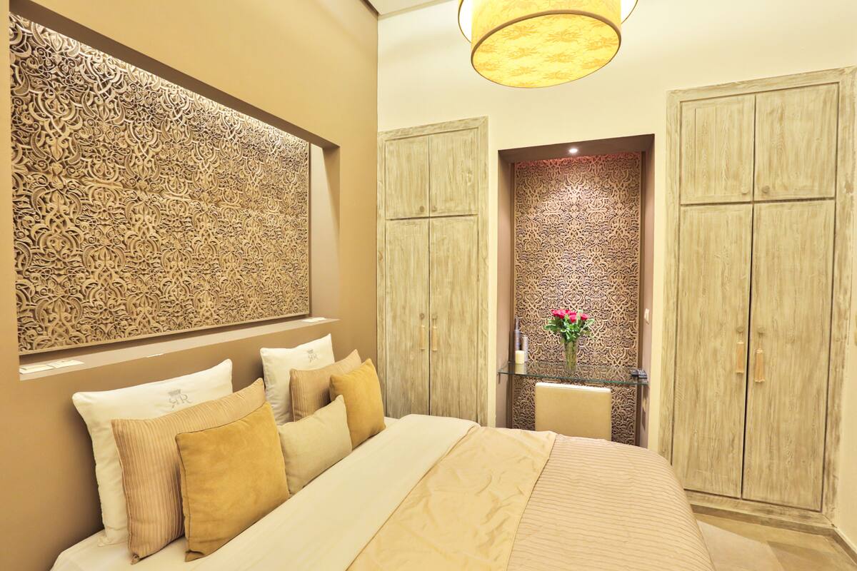 Un dormitorio con una cama grande, un panel decorativo en la pared, un armario de madera y una mesita con un florero.
