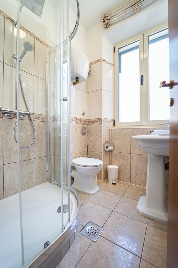 A modern bathroom with a glass-enclosed shower, a toilet, a sink, and a window providing natural light.
