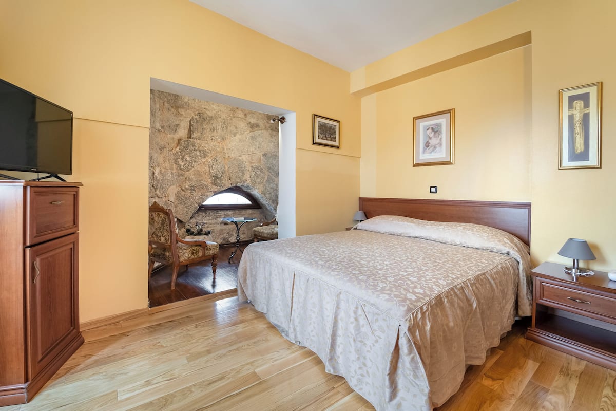 A bedroom with a bed, wooden furniture, a stone wall, and framed pictures on the wall.