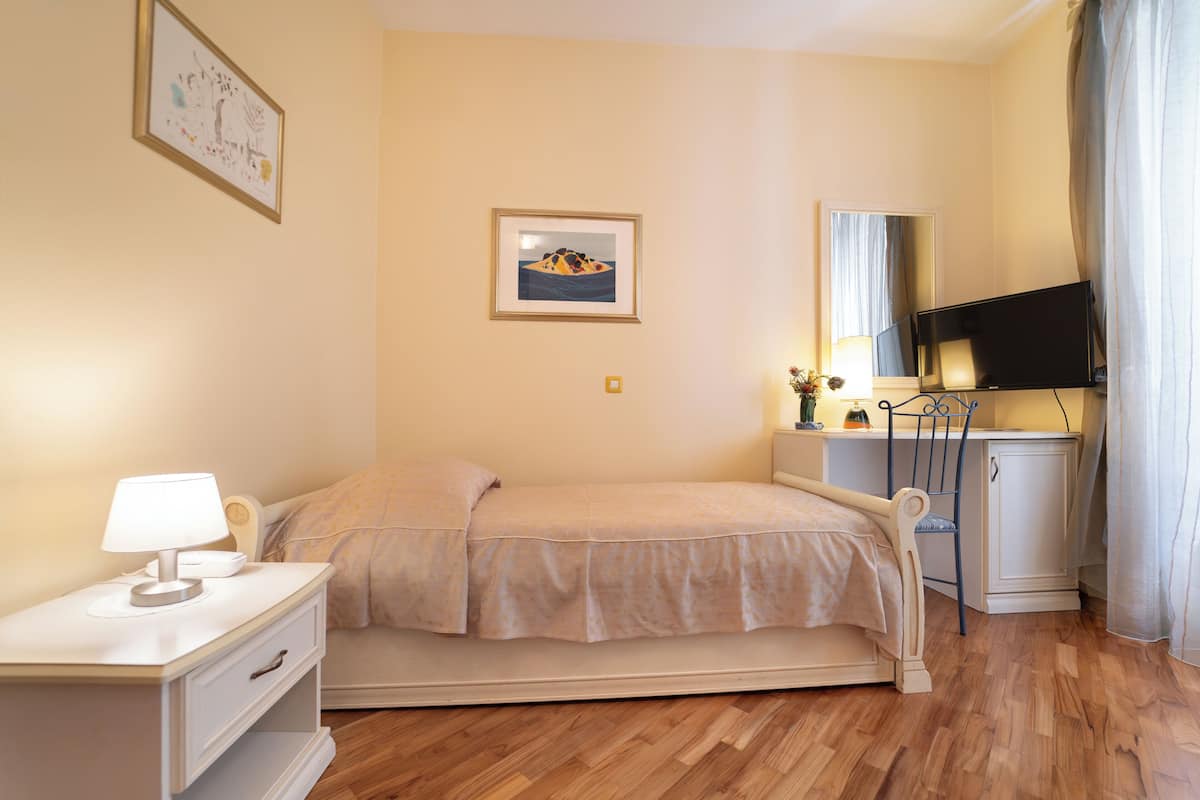 A bedroom with a bed, bedside table, lamp, TV, and a framed picture on the wall.