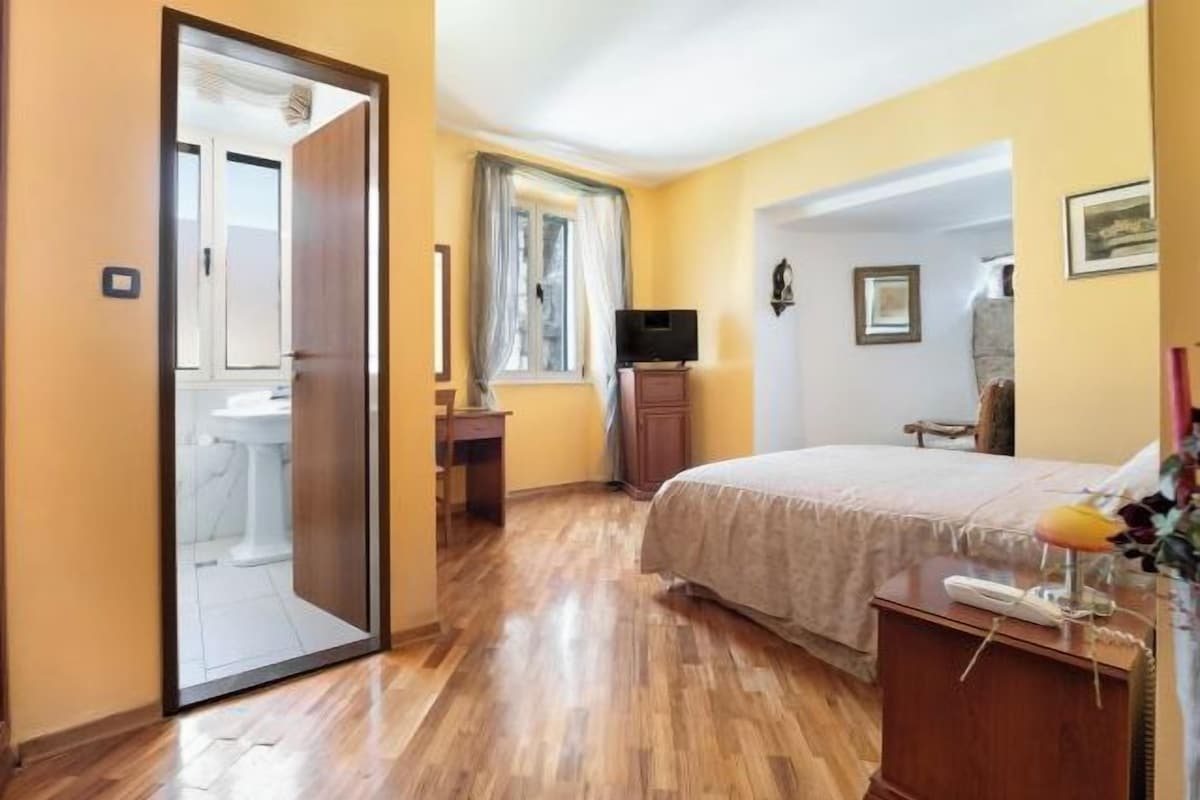Une chambre avec un plancher en bois, un lit, un bureau, une chaise, une télévision et une armoire.